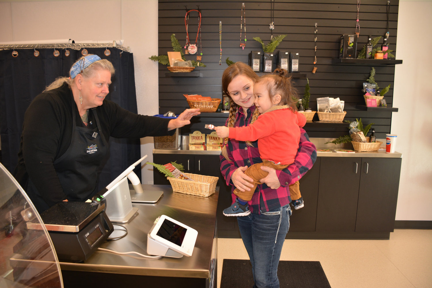 From left, Sue Bachmeier hands a candy to Keoni Jr. Kalama and his mother Krystan at the She Nah Nam Seafood retail store.