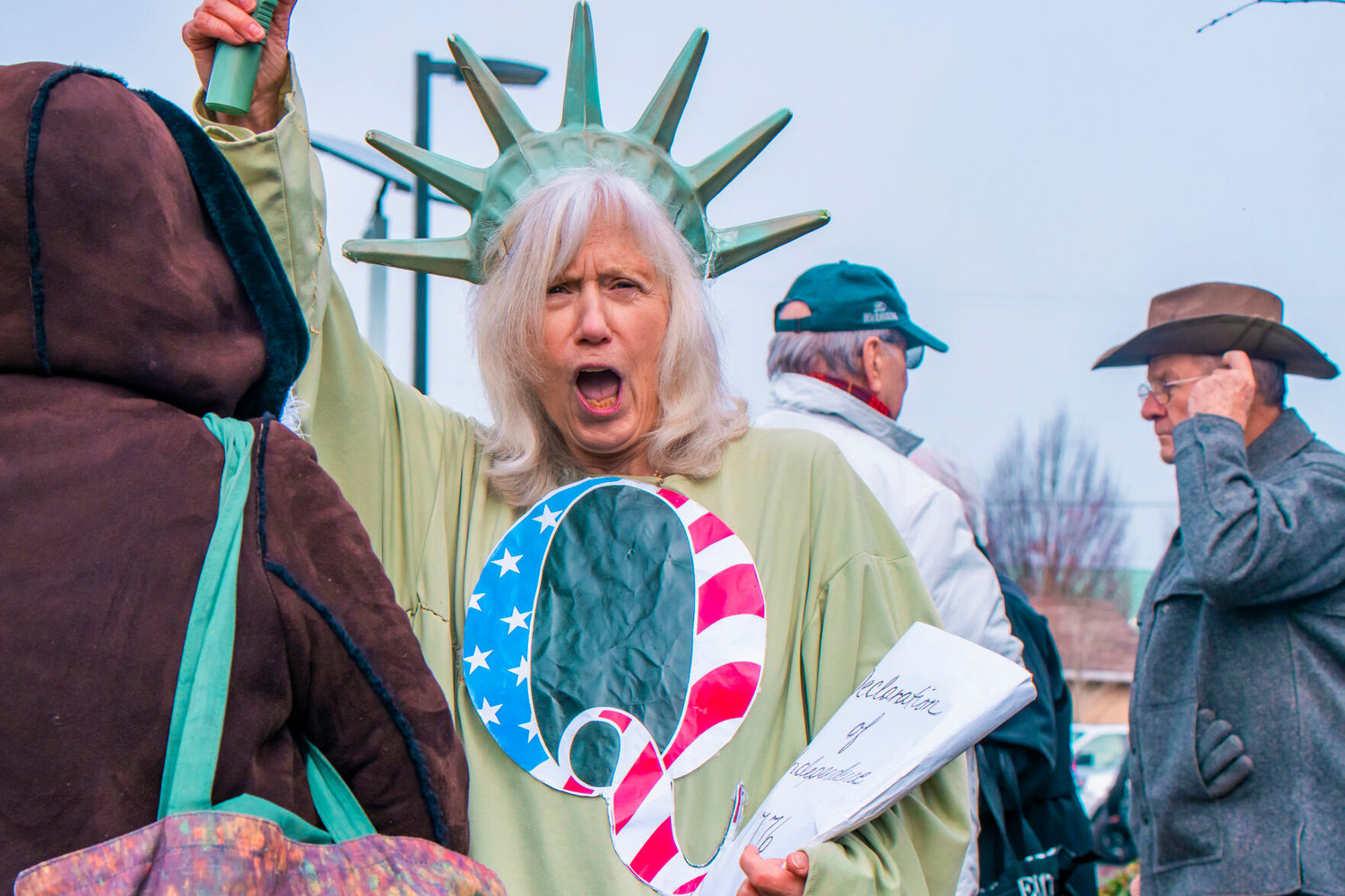 A woman dressed as the Statue of Liberty sports a ‘Q’ on her chest during a protest to ‘Open Yelm Now’ at Yelm City Park on Saturday.