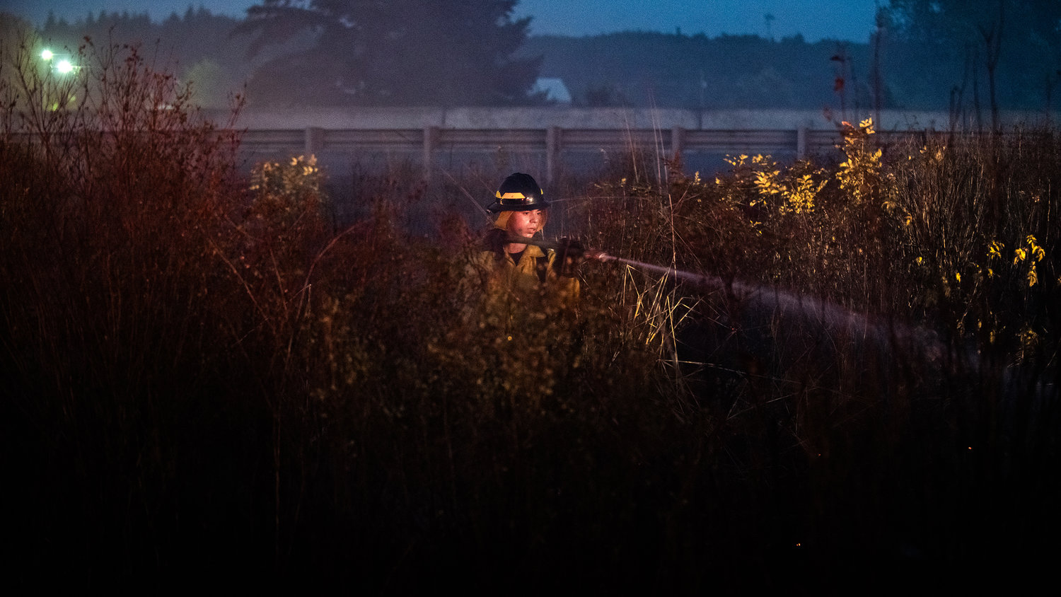 A firefighter uses a hose to extinguish flames near Interstate 5 Thursday night in Grand Mound.