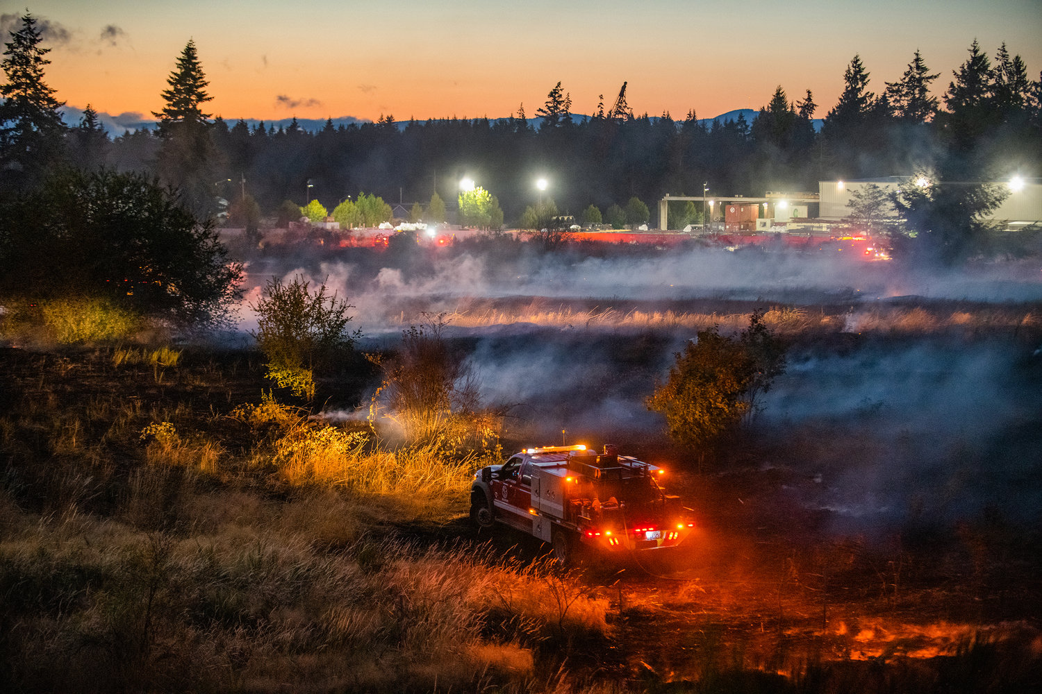 Smoke is illuminated by lights on a truck as hoses stretch across a field between Elderberry Street Southwest and Interstate 5 Thursday night at milepost 88 in Grand Mound.