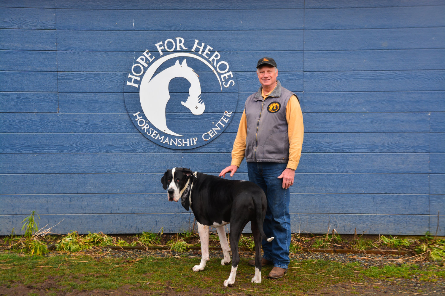Bob Woelk poses with his dog Junior in front of a Hope for Heroes sign on a tack room in Yelm.