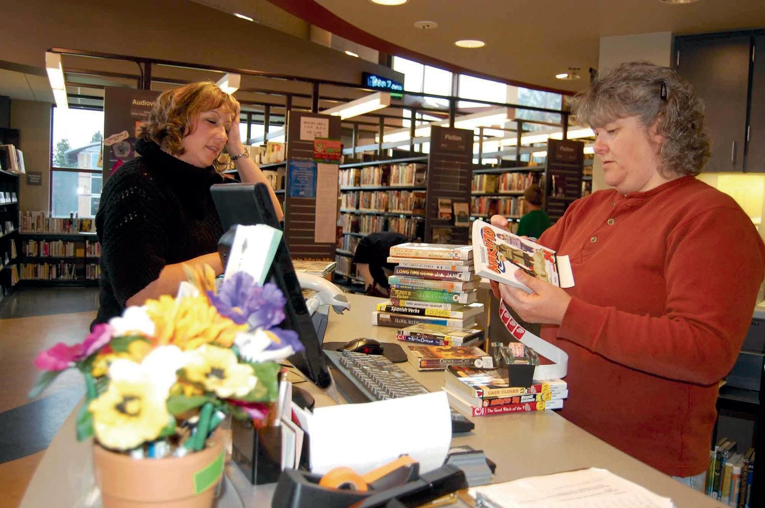 Linda Davis of Yelm, left, asks library aide Jody Renu a question after checking out a stack of library book in this file photo.