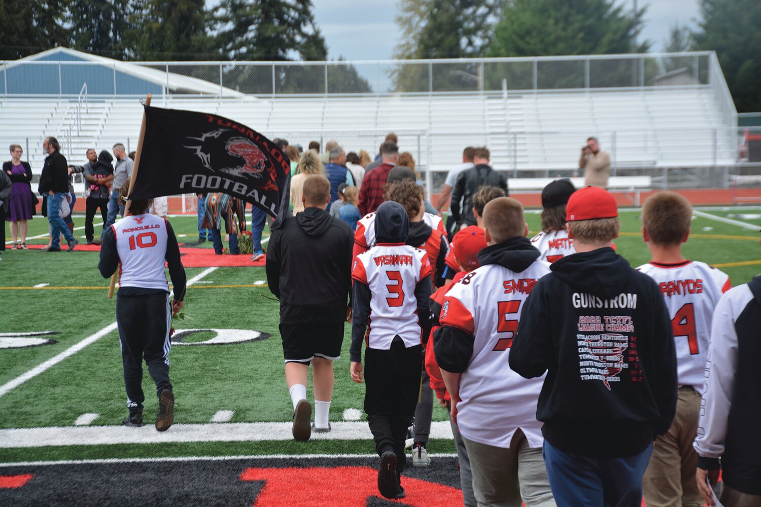 Members of Shawn Jemtegaard’s TCYFL team enter the field to place their roses during a memorial service on May 21.