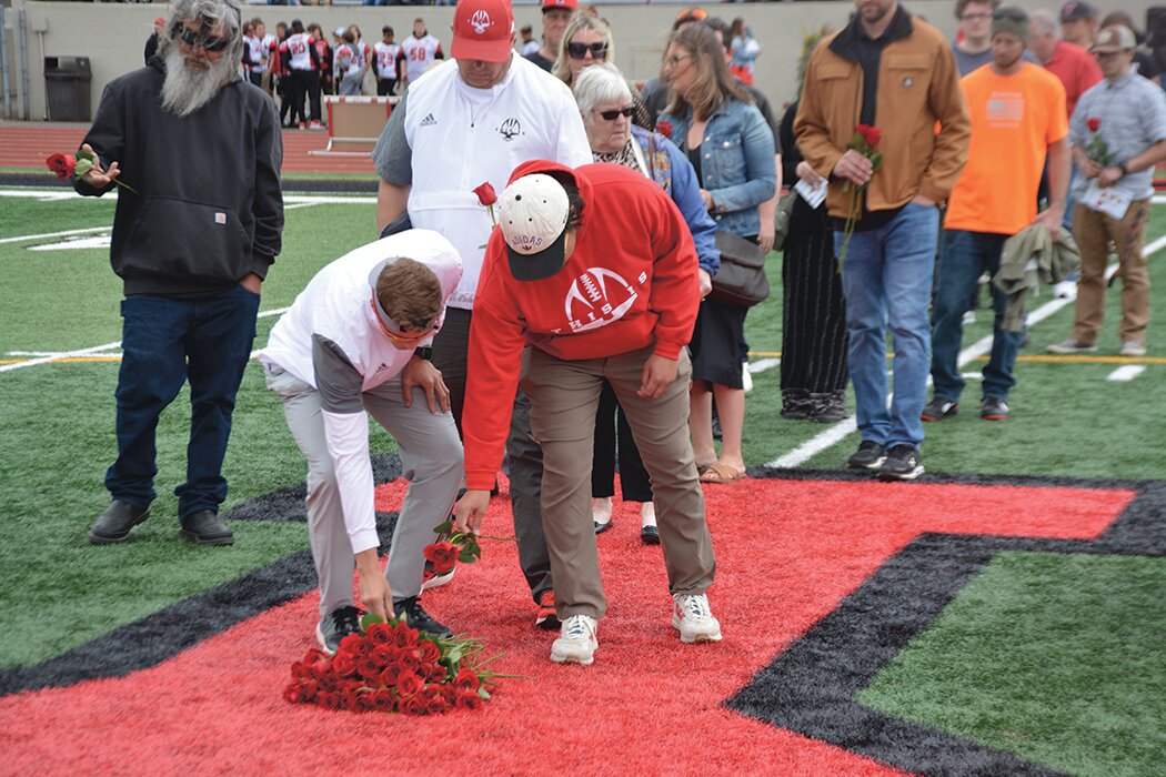 Yelm coaches Jacob Nolan and Brandon Thompson place roses on the field in honor of Shawn Jemtegaard, who was killed in April.