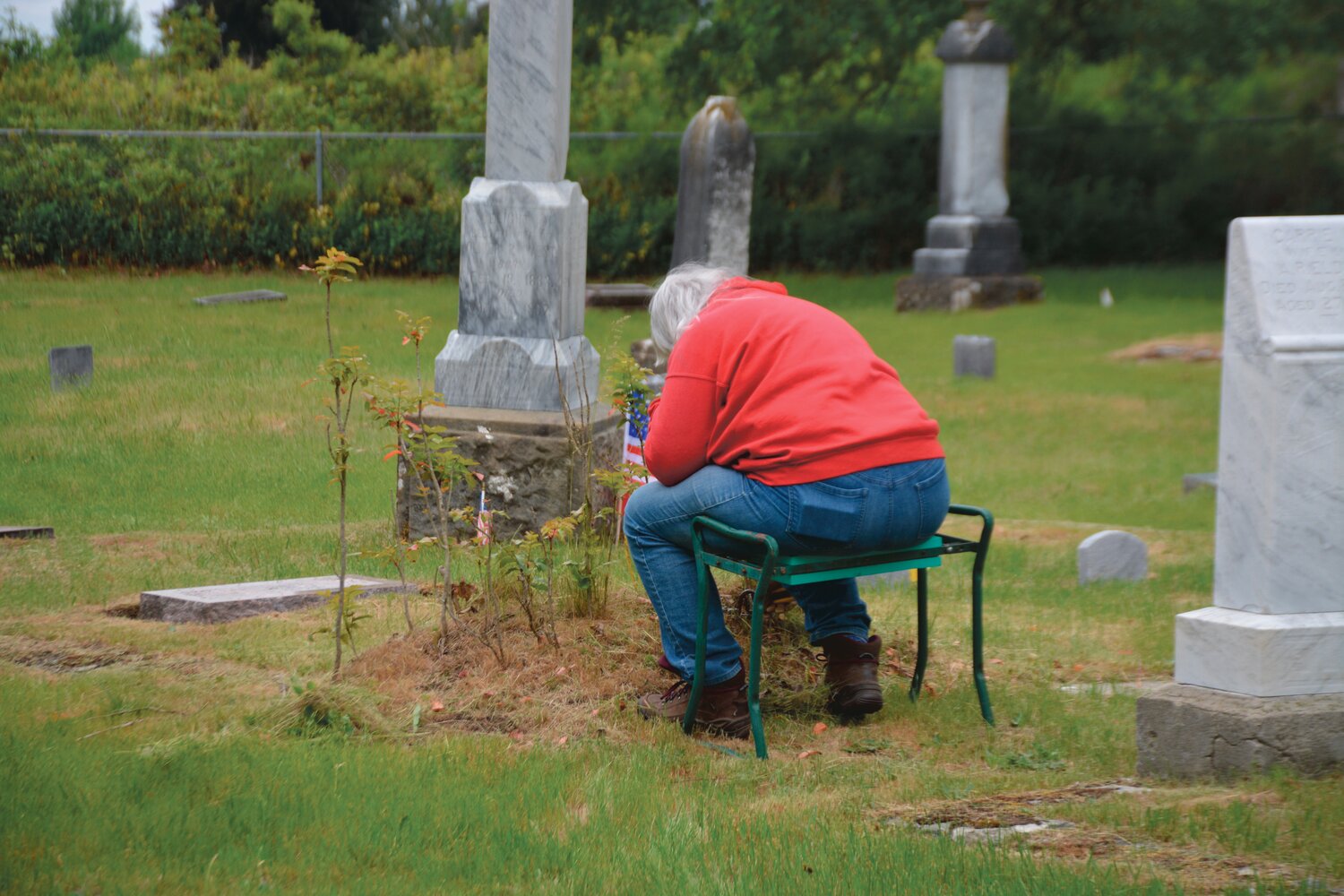 A volunteer trims the grass near a gravesite at the Roy Cemetery on Sunday, May 21.