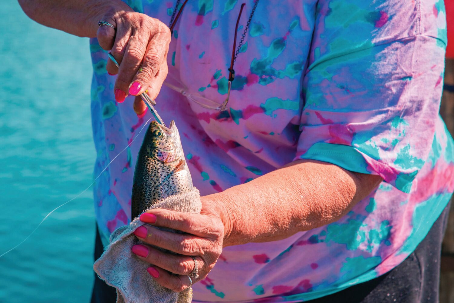 Terry Todd, of Sumner, holds a rainbow trout as she works to remove a hook while fishing at Deep Lake at Millersylvania State Park in this file photo.