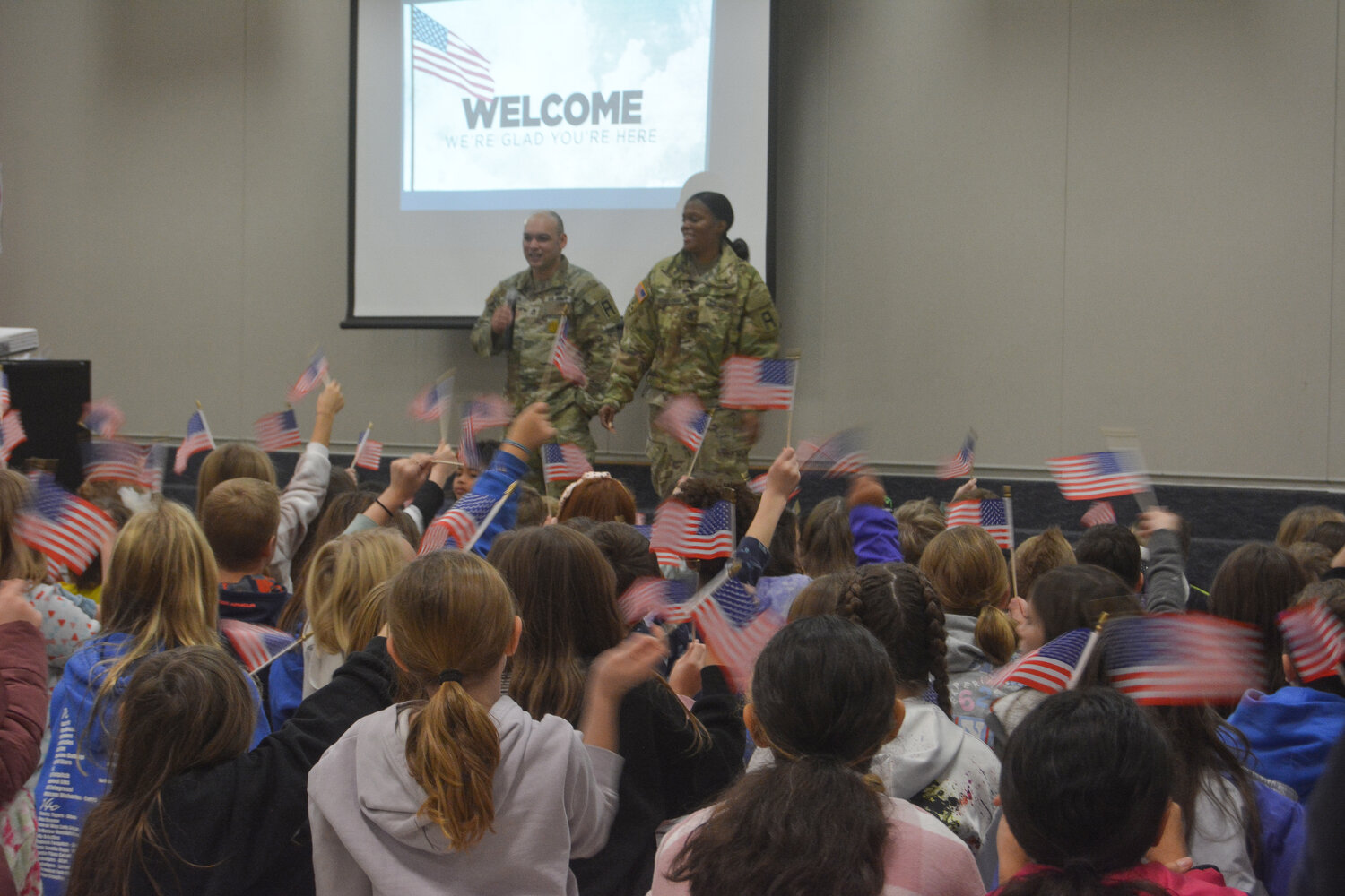 Roy Elementary students wave American flags as Sgt. First Class Ryan Lawless and Sgt. First Class Unique McDowell-Edwards speak at a Nov. 9 assembly.
